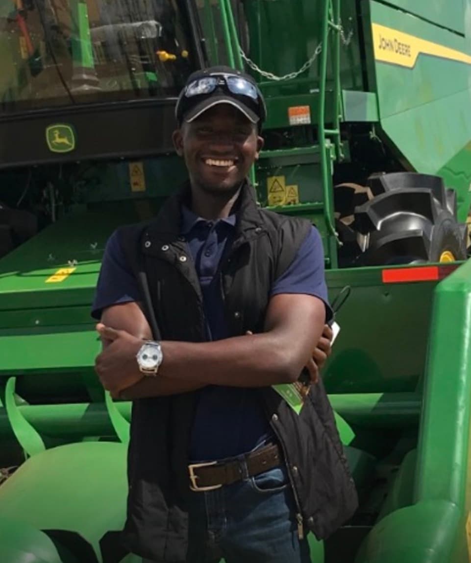 Ernest Kapesa, founder and CTO of Agririgo, standing in front of a combine harvester