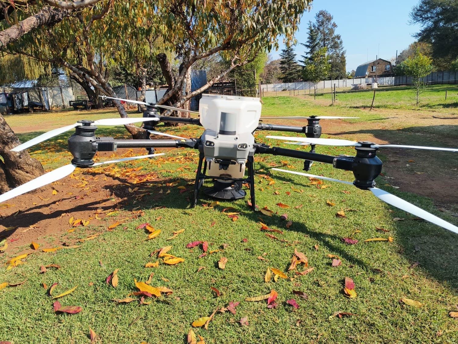 An agricultural spray drone on grass, arms unfolded, ready to fly